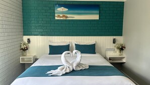 Habitació d'hotel amb llit, paret d'accent color cel, roba de llit blanca, dues mesetes de nit amb làmpades i un quadre amb una escena de platja.