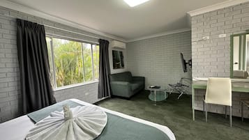 Een hotelkamer met een bed, een bureau, een stoel, een bank, een televisie en een raam met gordijnen.