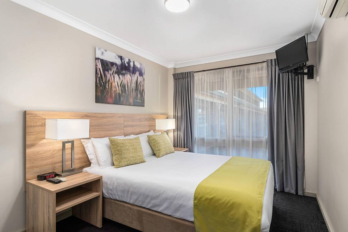 A hotel room with a bed, bedside lamps, a TV, and a window with curtains.