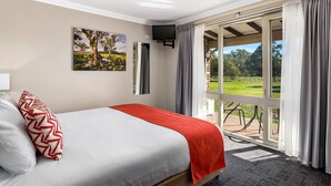 Una habitación de hotel con cama, un cuadro, un televisor y vistas a un jardín.