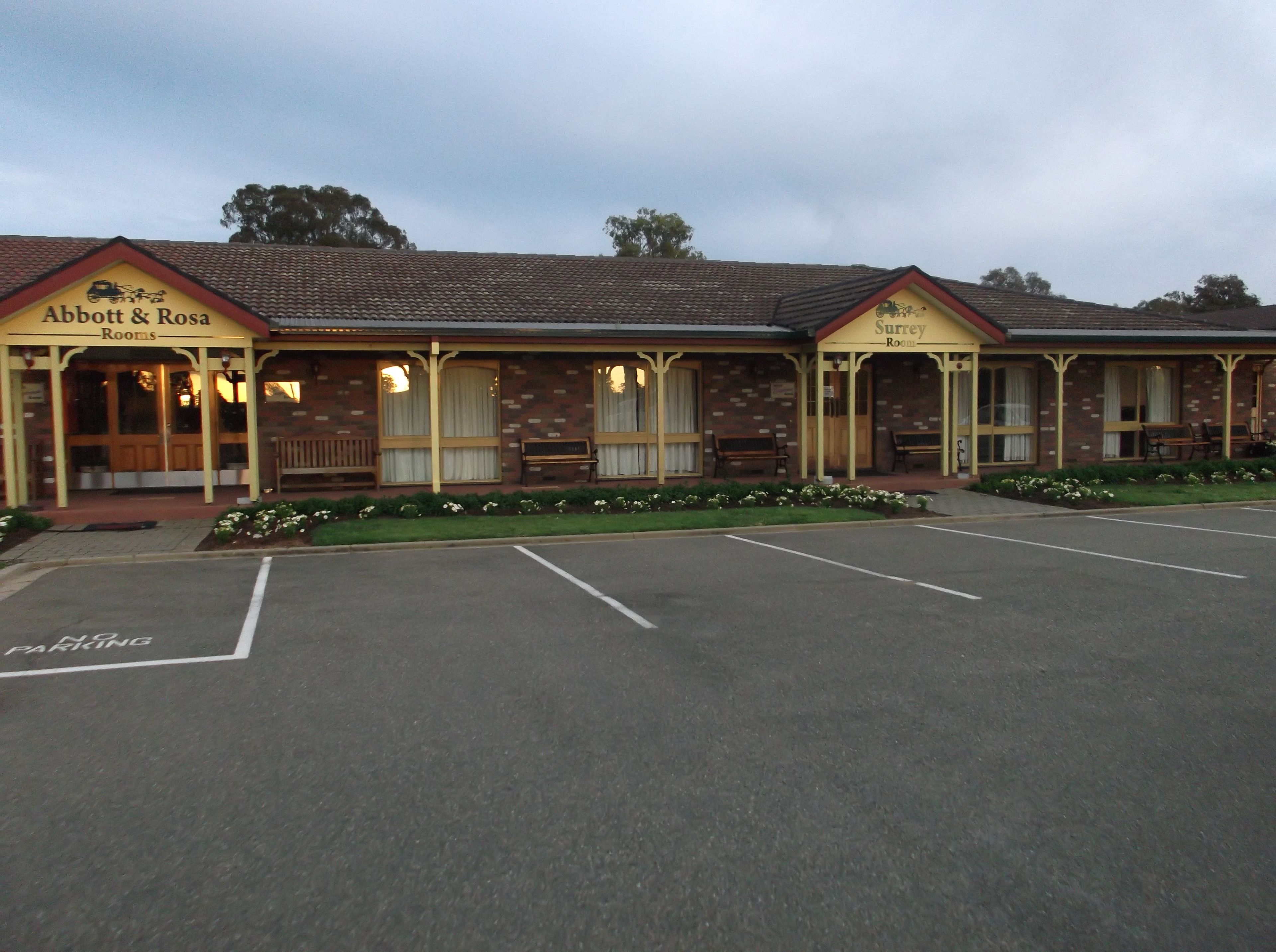 A building with two sections labeled "Abbott & Rosa Rooms" and "Surrey Rooms". There is a parking lot in front.