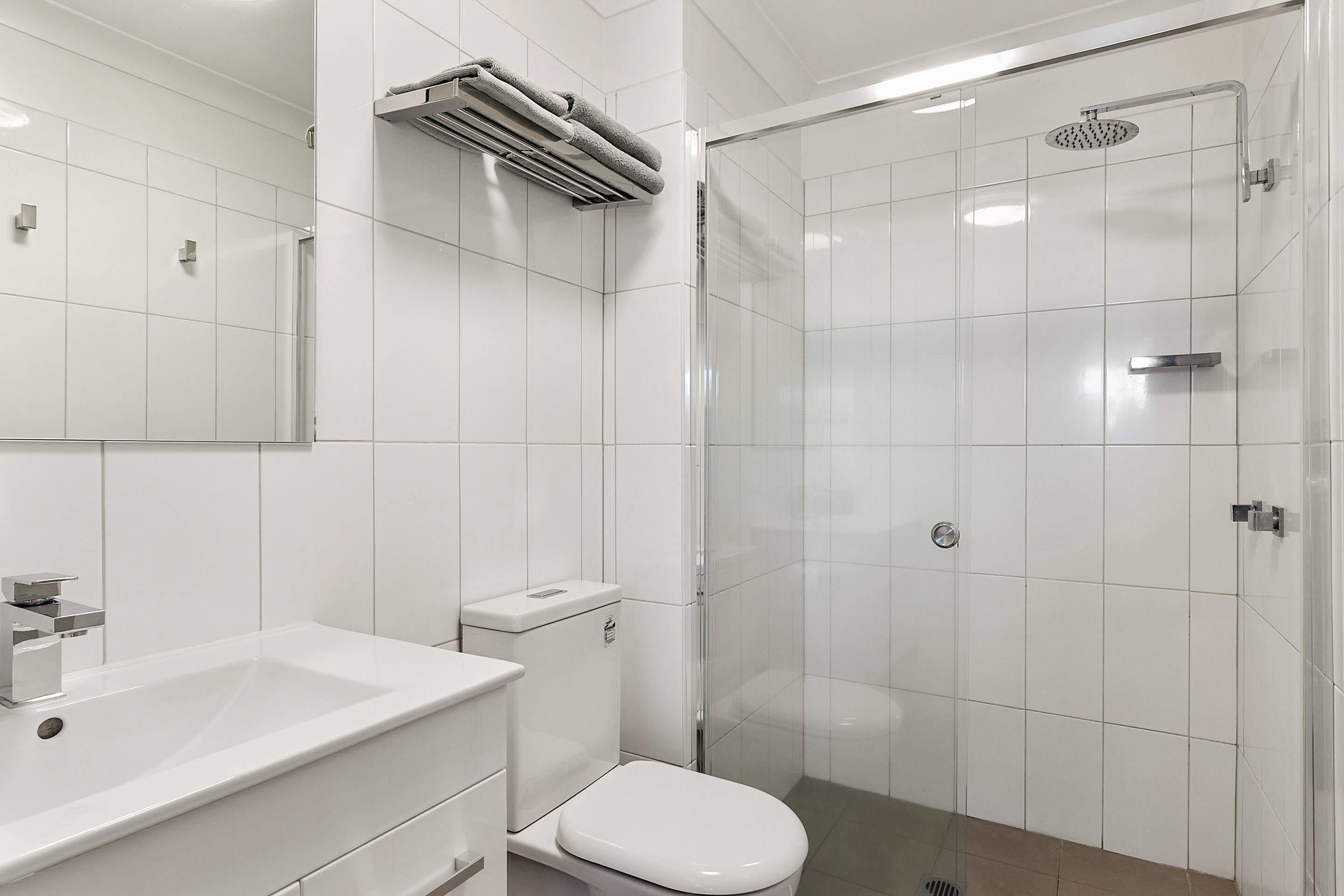 Un baño moderno con lavamanos, inodoro y zona de ducha blancos.