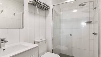 Un baño moderno con lavamanos, inodoro y zona de ducha blancos.