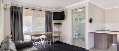 Una sala de estar moderna con un sofá, una mesa de comedor con sillas, un televisor de pantalla plana y una cocina con pileta y alacenas.