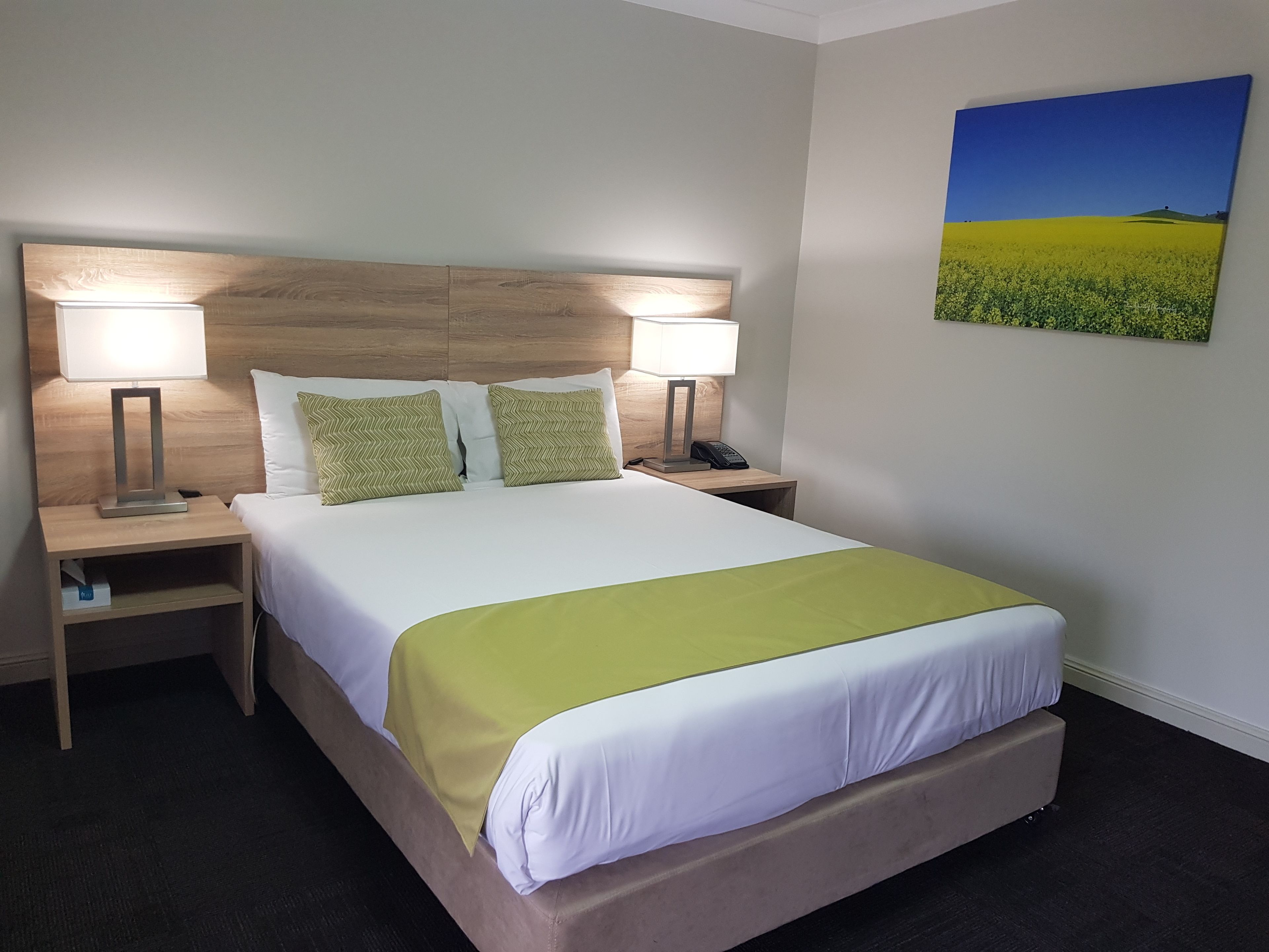 A hotel room with a bed, two bedside tables, two lamps, a telephone, and a painting on the wall.