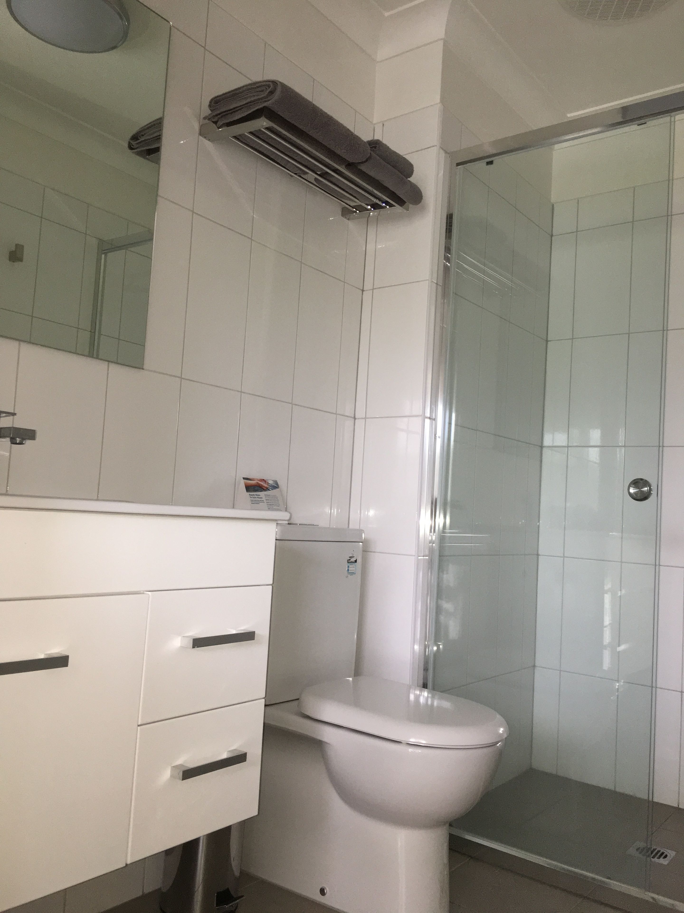 A bathroom with a white toilet, a glass shower enclosure, and a white vanity with drawers.