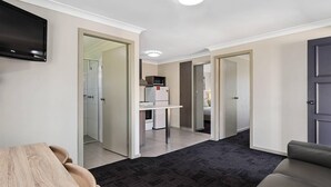 Una sala de estar moderna con televisor de pantalla plana, una mesa de comedor, un sofá y una cocina visible a través de una puerta abierta.