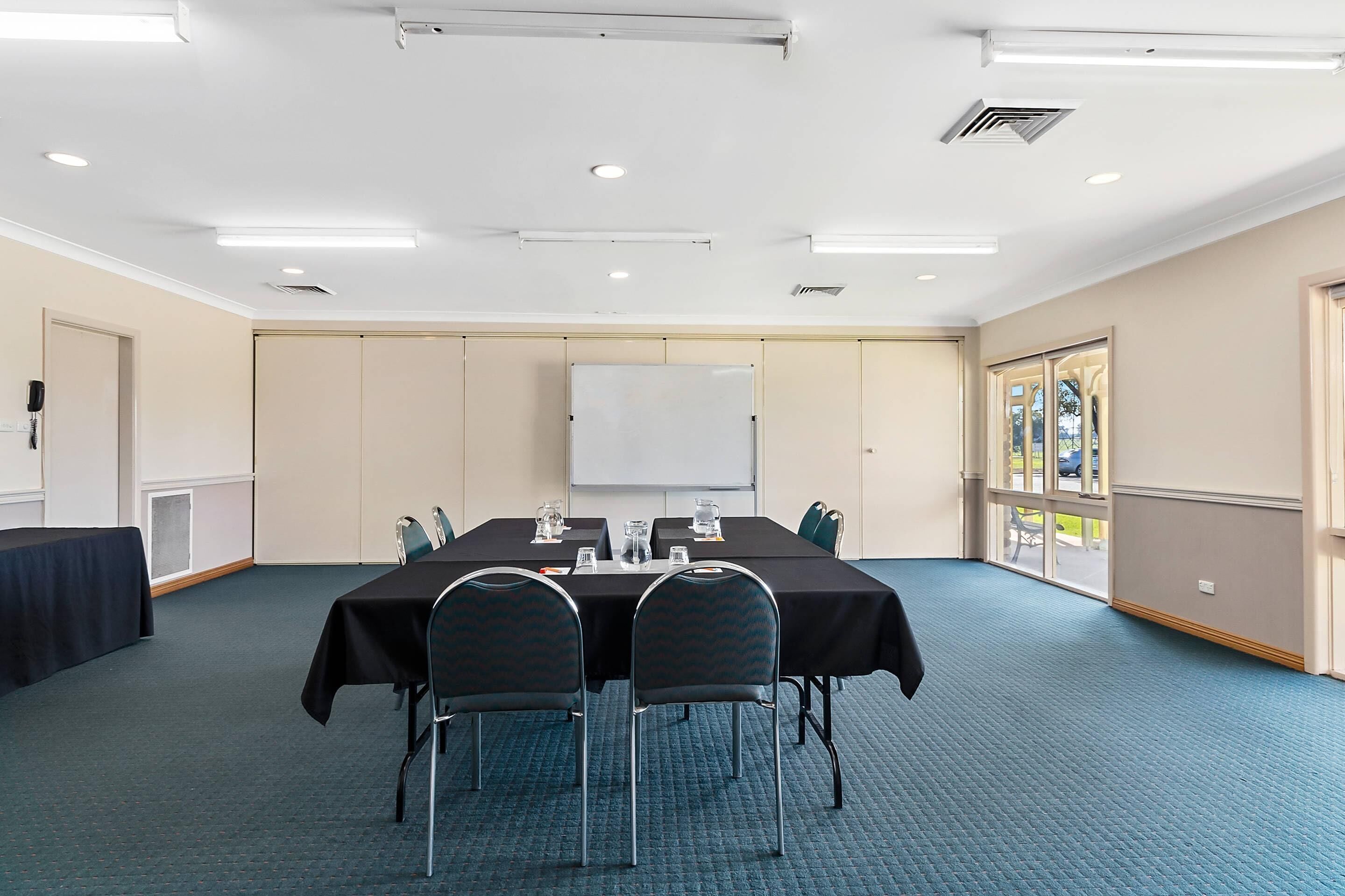 A conference room with a long table, chairs, a whiteboard, and a window with a view.