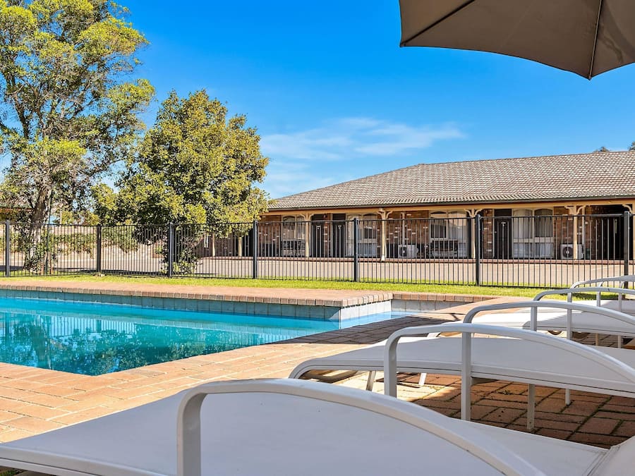 A swimming pool with lounge chairs, a covered patio, and a building with a tiled roof.