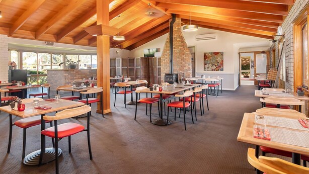 Un restaurante con mesas de madera, sillas rojas, una chimenea de ladrillo y ventanas amplias.