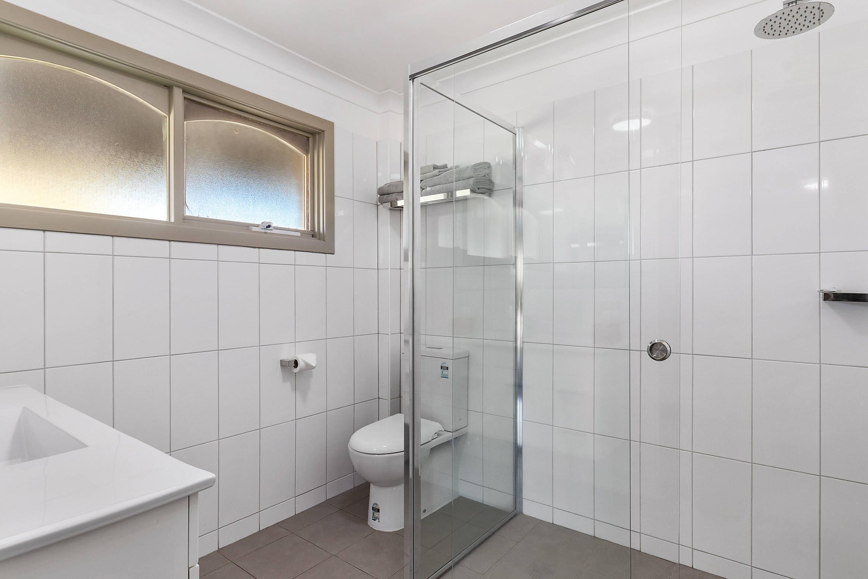 A bathroom with a glass-enclosed shower, a toilet, and a sink.
