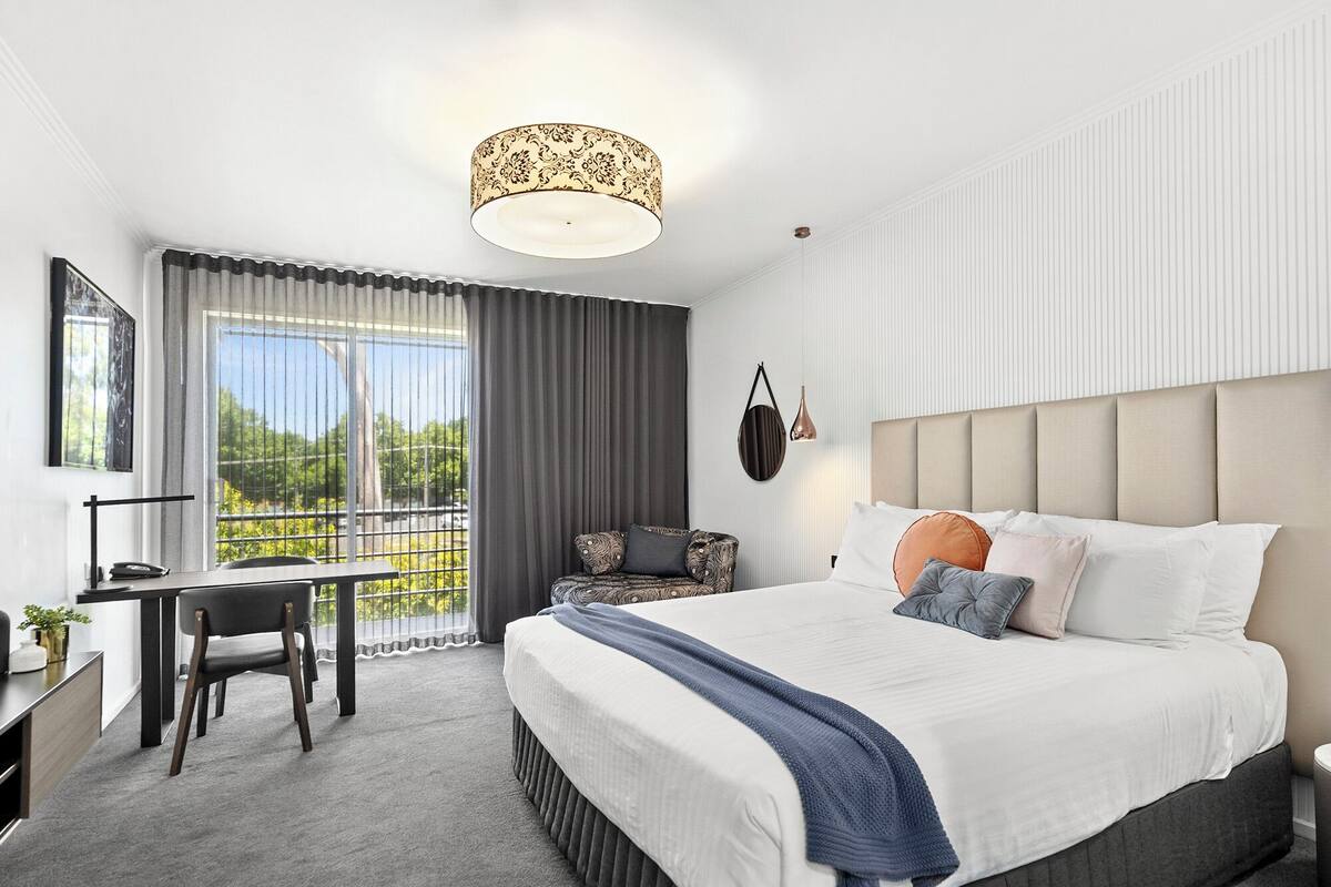 A modern hotel room with a large bed, a desk, and a view of the outdoors.
