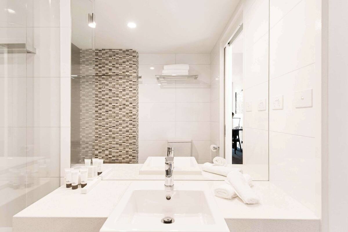 A modern bathroom with a large mirror, two sinks, and a shower area.