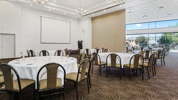 Un salón de conferencias con mesas redondas, sillas, una pantalla de proyector y un atril.