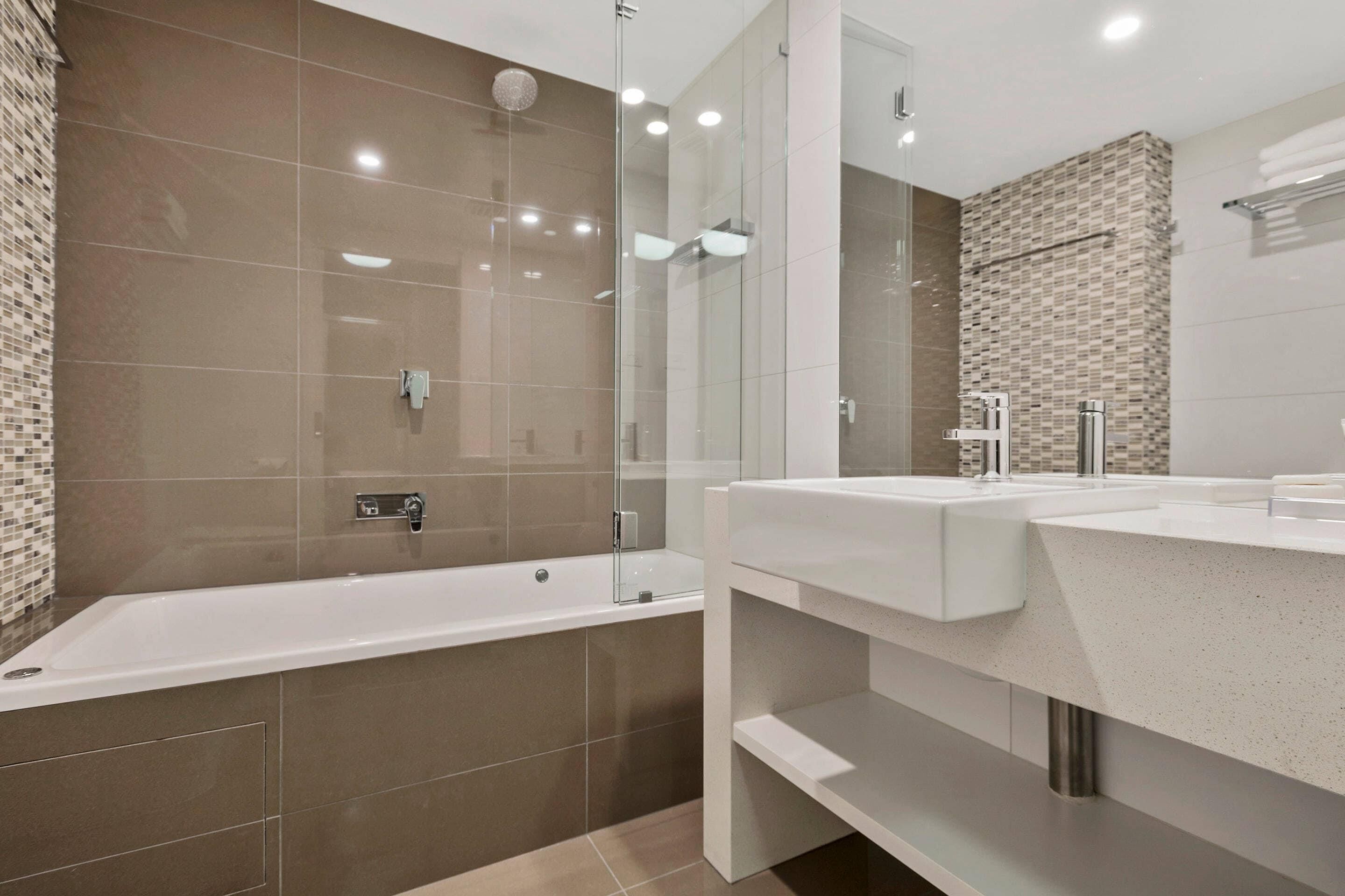 Un bagno moderno con doccia a vetro, vasca da bagno bianca e mobile lavabo doppio.