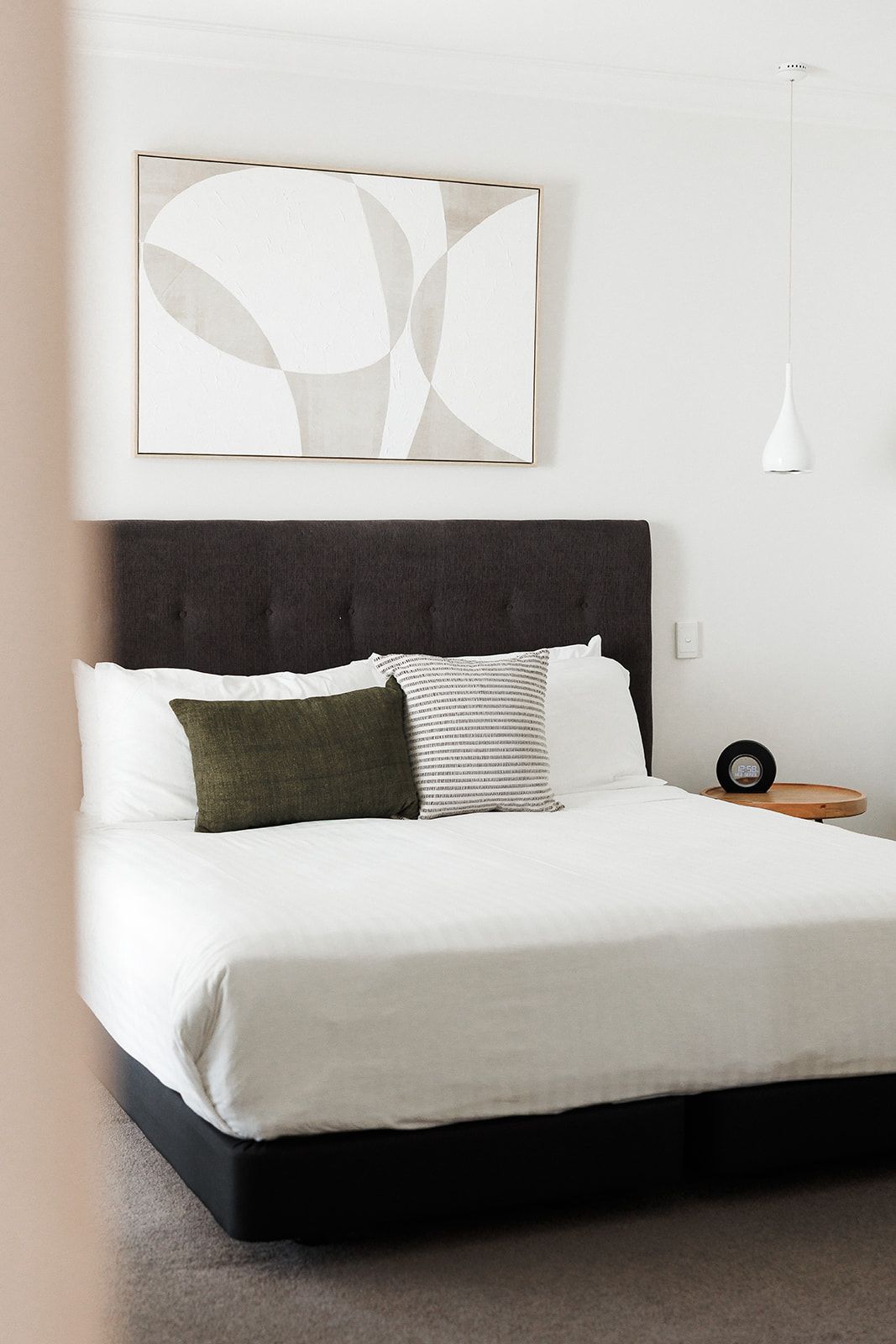A bedroom with a bed, a headboard, a bedside table, a clock, and a wall-mounted light fixture.
