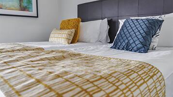 Una cama bien hecha con una colcha estampada, un cabecero oscuro y varias almohadas con diferentes diseños y colores.