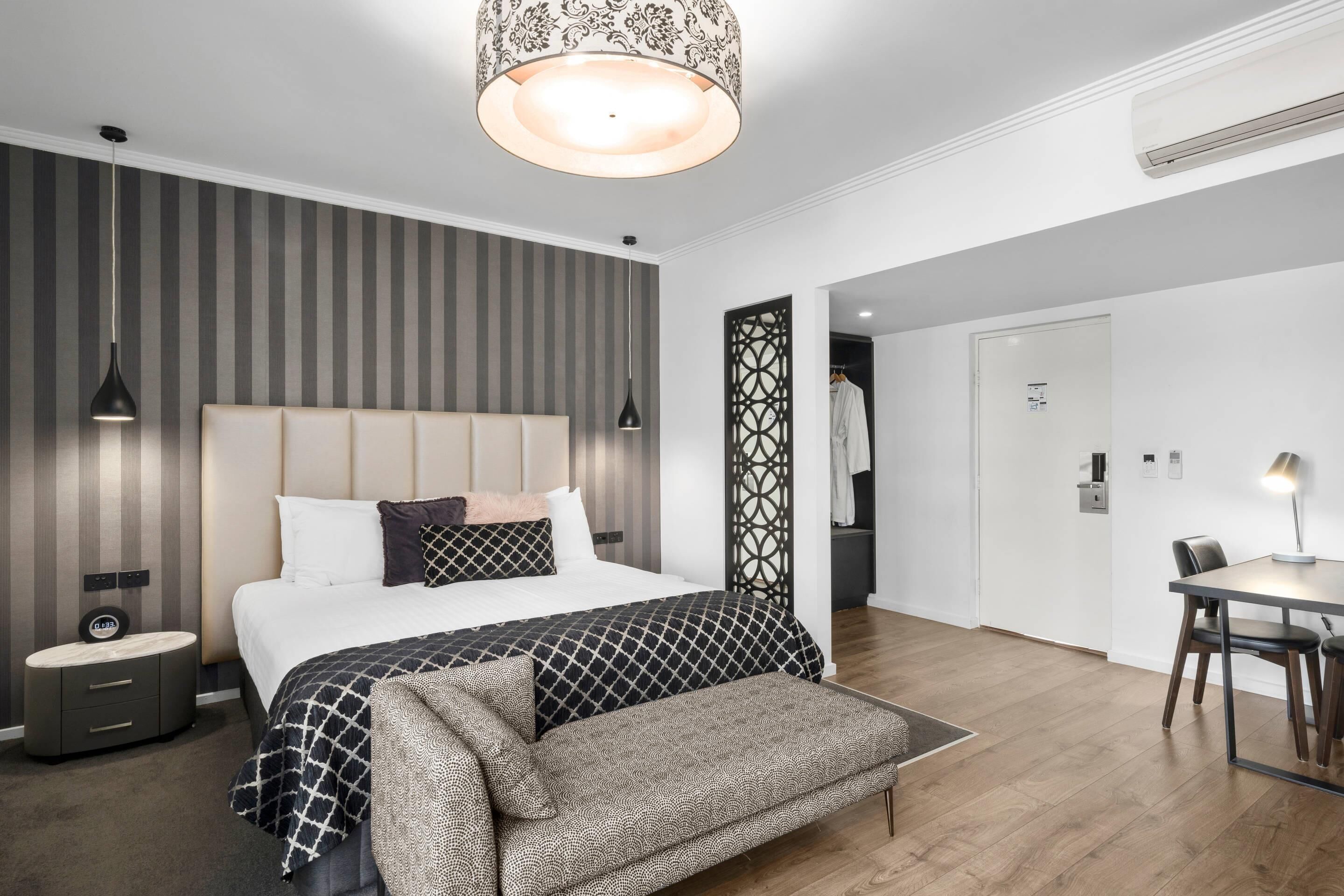 A modern bedroom with a large bed, bedside tables, a bench, a dining area with a table and chairs, and a decorative partition.
