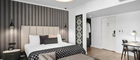 A modern bedroom with a large bed, bedside tables, a bench, a dining area with a table and chairs, and a decorative partition.
