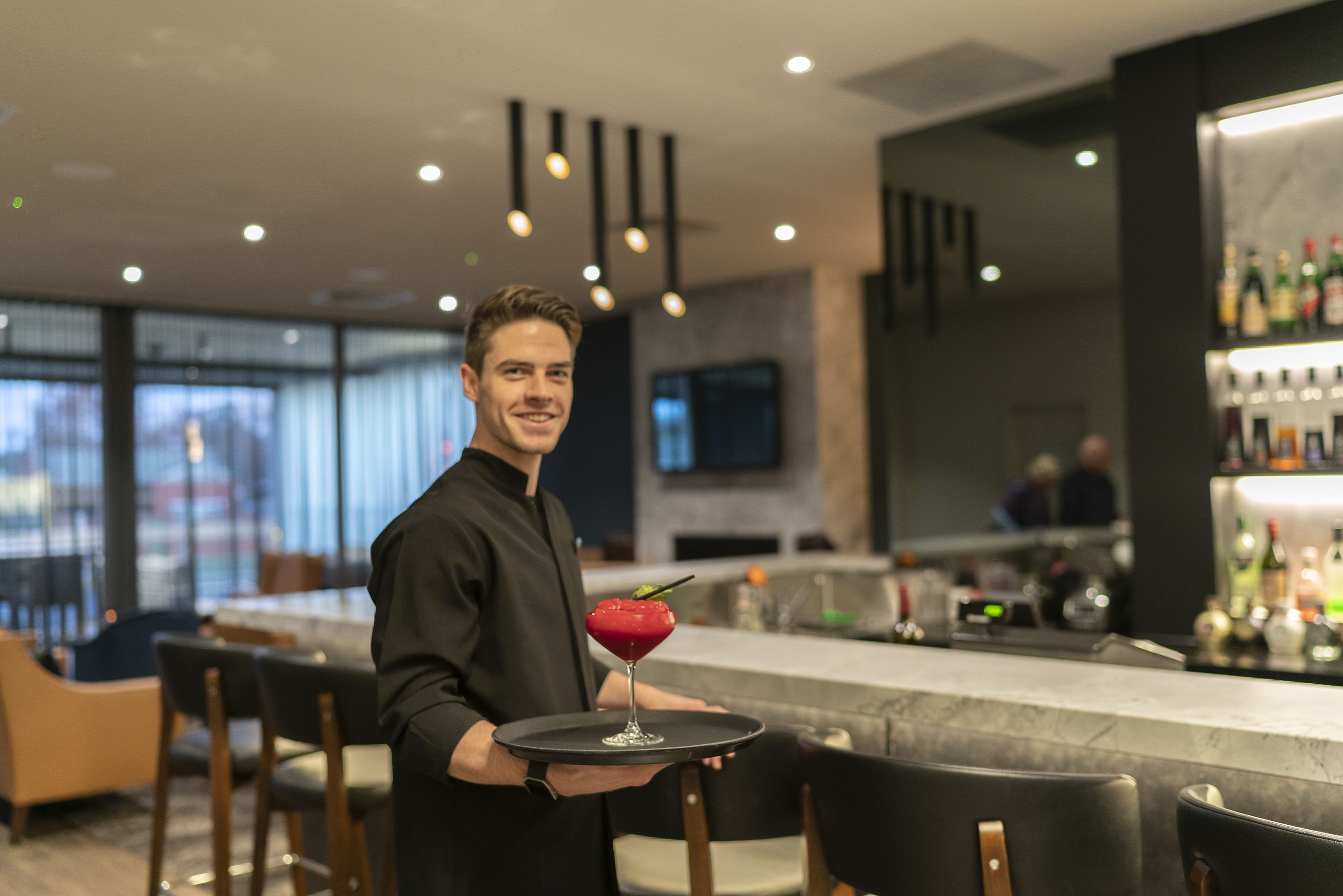 En person som håller ett bricka med en drink i en modern bar.