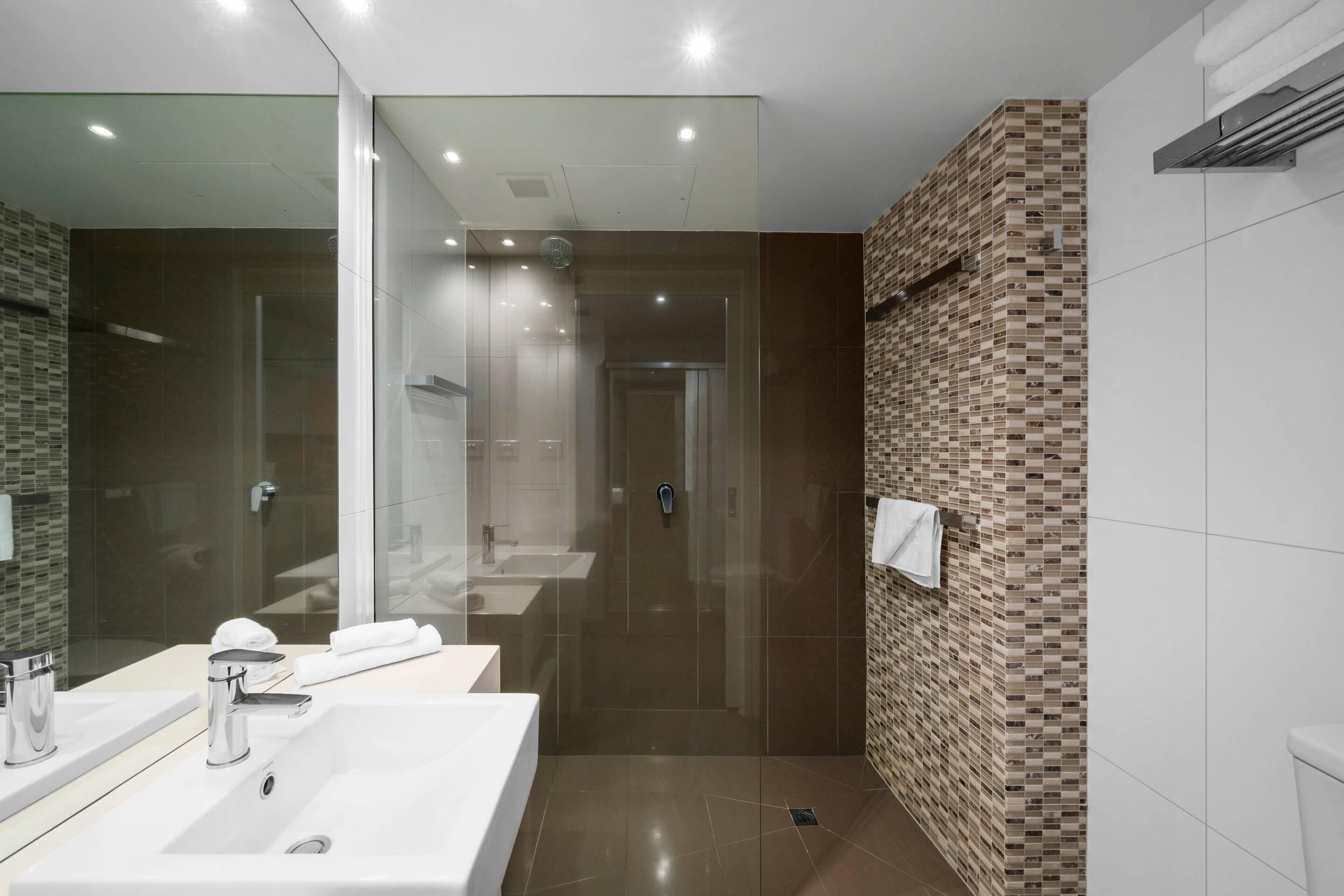 Un baño moderno con ducha envuelta en vidrio, un espejo grande y pared de azulejos.