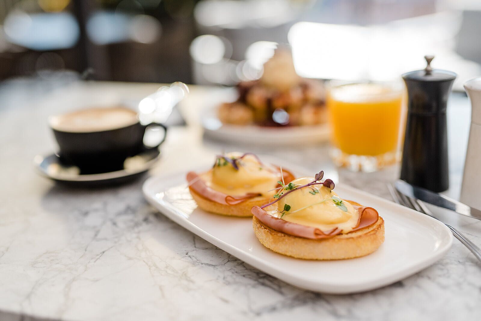 A breakfast setting with two English muffins topped with ham and cheese, a cup of coffee, and a glass of orange juice.