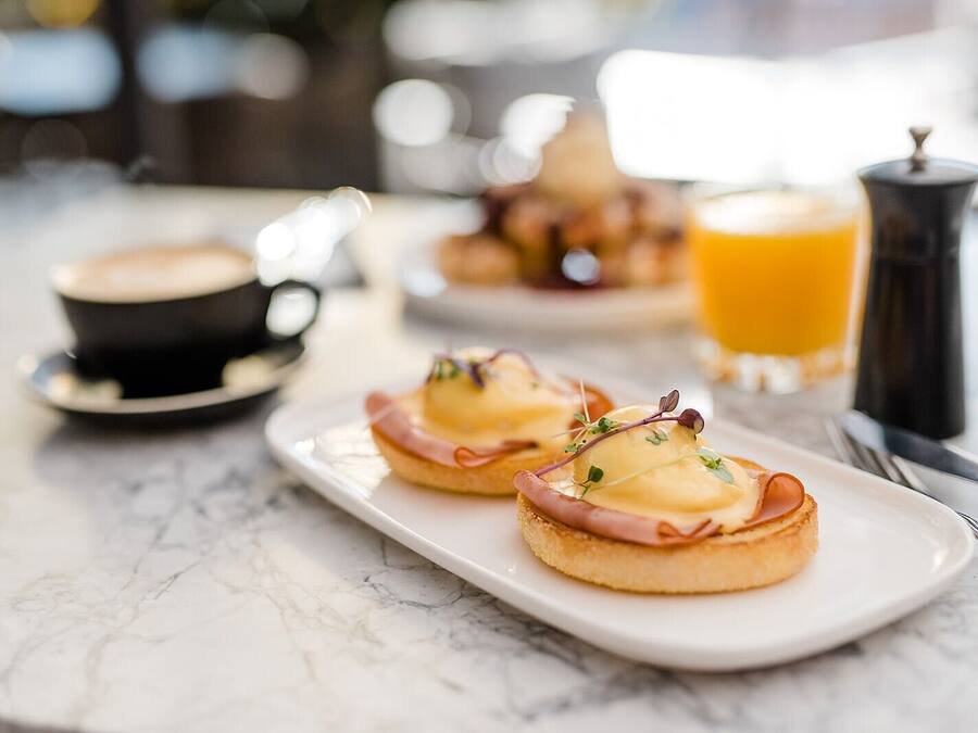 A breakfast setting with two English muffins topped with ham and cheese, a cup of coffee, and a glass of orange juice.