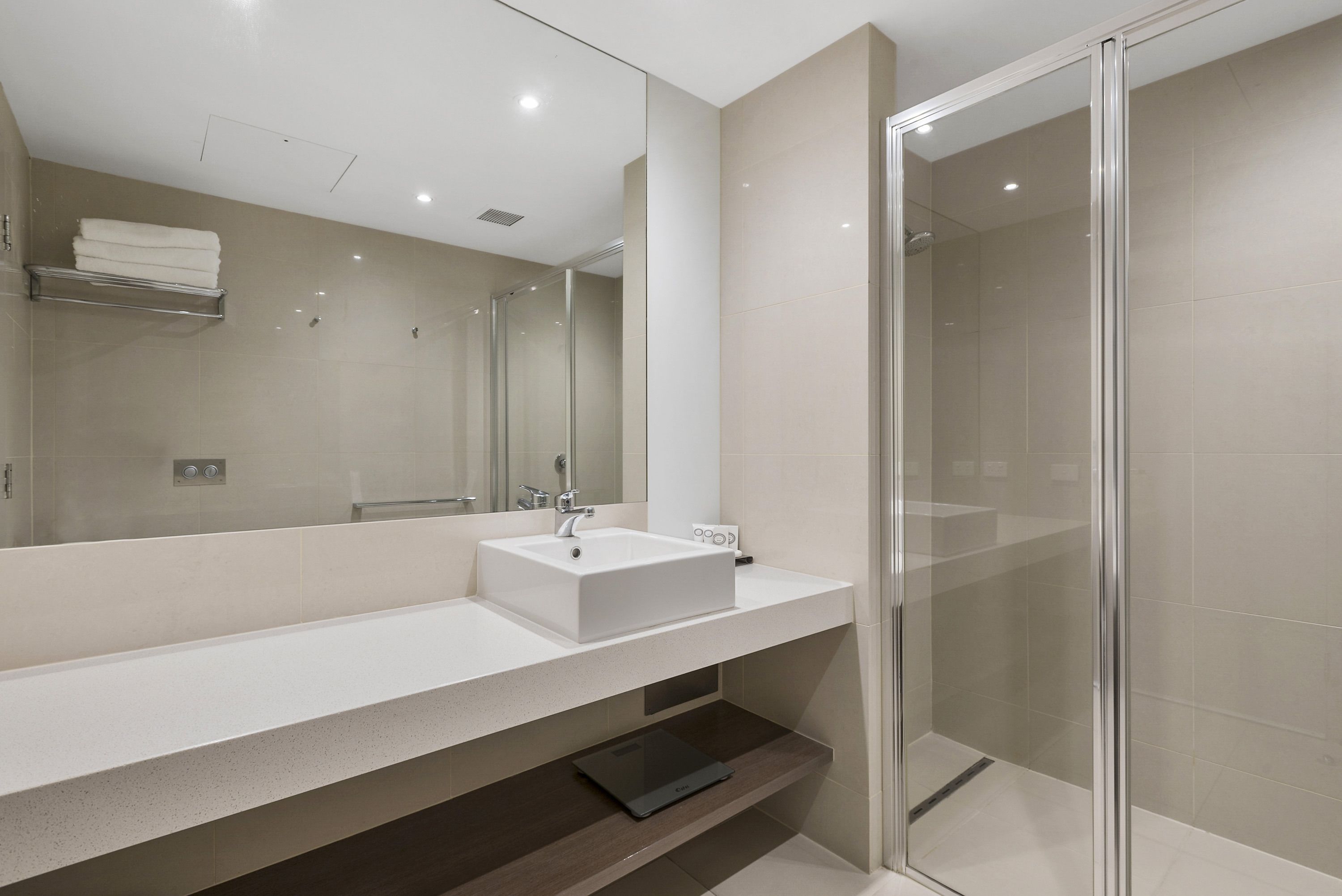 Un baño moderno con un espejo grande, un lavabo blanco y una cabina de ducha de vidrio.
