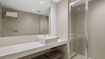 Un baño moderno con un espejo grande, un lavabo blanco y una cabina de ducha de vidrio.