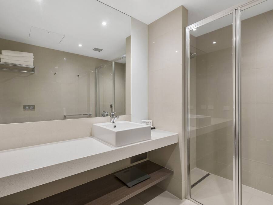 Un baño moderno con un espejo grande, un lavabo blanco y una cabina de ducha de vidrio.
