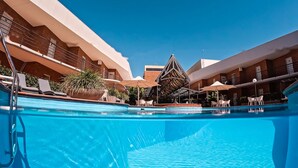 A swimming pool with lounge chairs and umbrellas, surrounded by hotel buildings with balconies and a distinctive triangular roof structure. - Quality Hotel Wangaratta Gateway (Wangaratta)