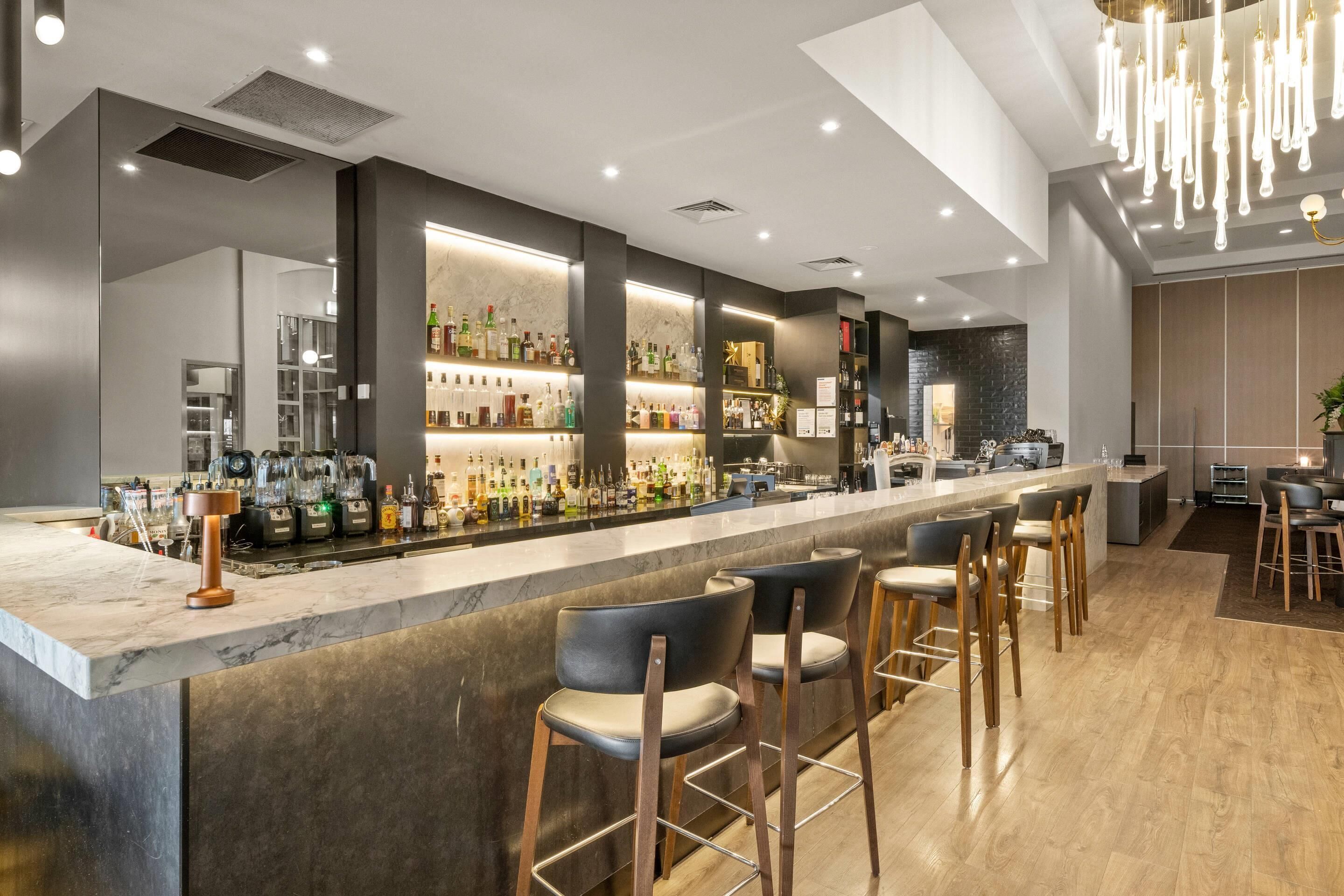 A modern bar area with a marble countertop, bar stools, and a variety of liquor bottles.