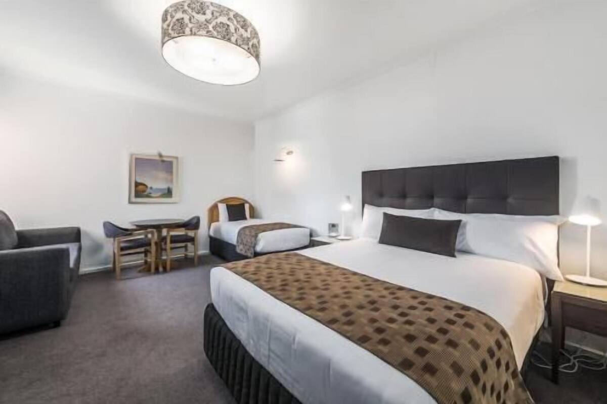 A hotel room with a bed, two bedside tables, a desk with a chair, a sofa, and a patterned ceiling light.