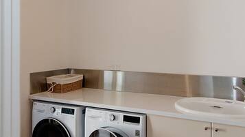 A laundry room with two front-loading washing machines, a stainless steel sink, and a basket on the countertop.