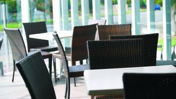 Des chaises et des tables en osier sur une terrasse extérieure, avec une rambarde en verre et vue sur la rue.
