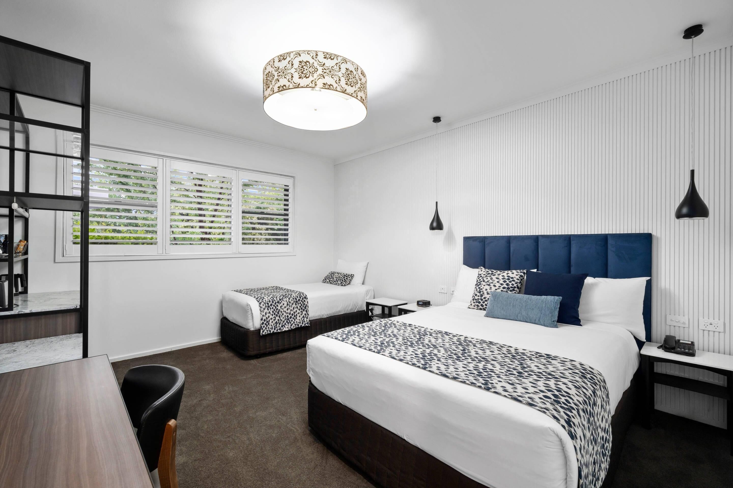 Quarto de hotel moderno com uma cama grande, uma cama menor, uma escrivaninha e uma cadeira.