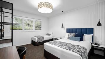 Quarto de hotel moderno com uma cama grande, uma cama menor, uma escrivaninha e uma cadeira.
