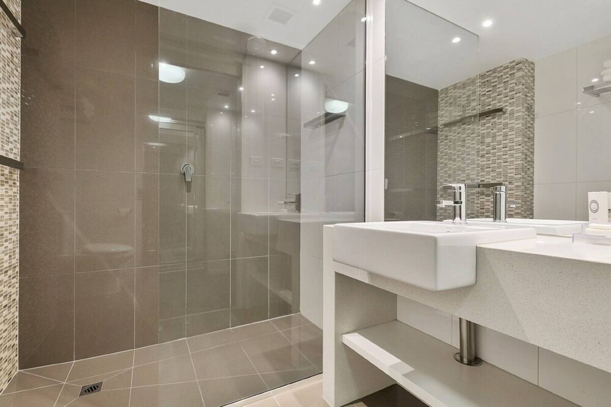 A modern bathroom with a glass-enclosed shower, a white sink, and a mirror.