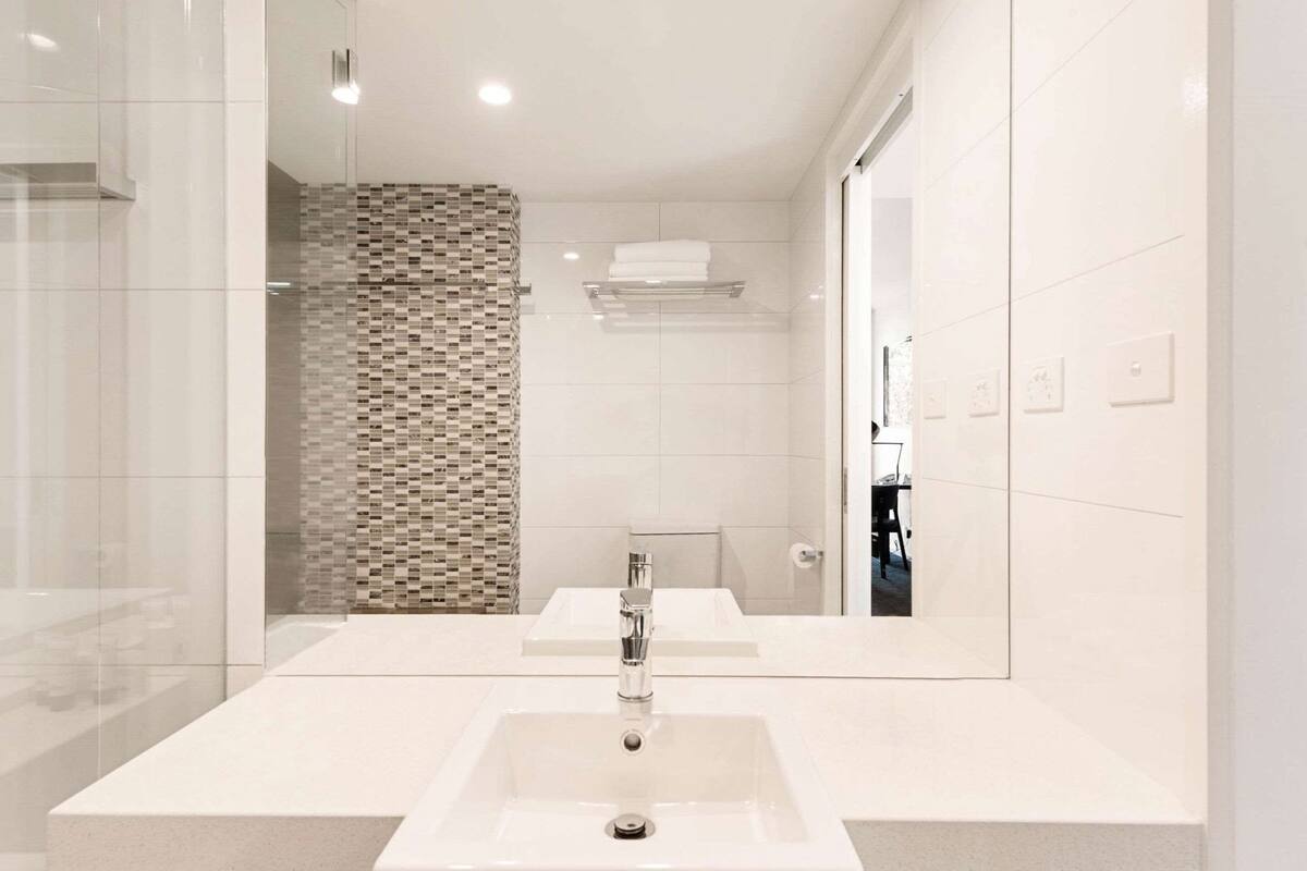 A modern bathroom with a large mirror, two sinks, and a tiled shower area.