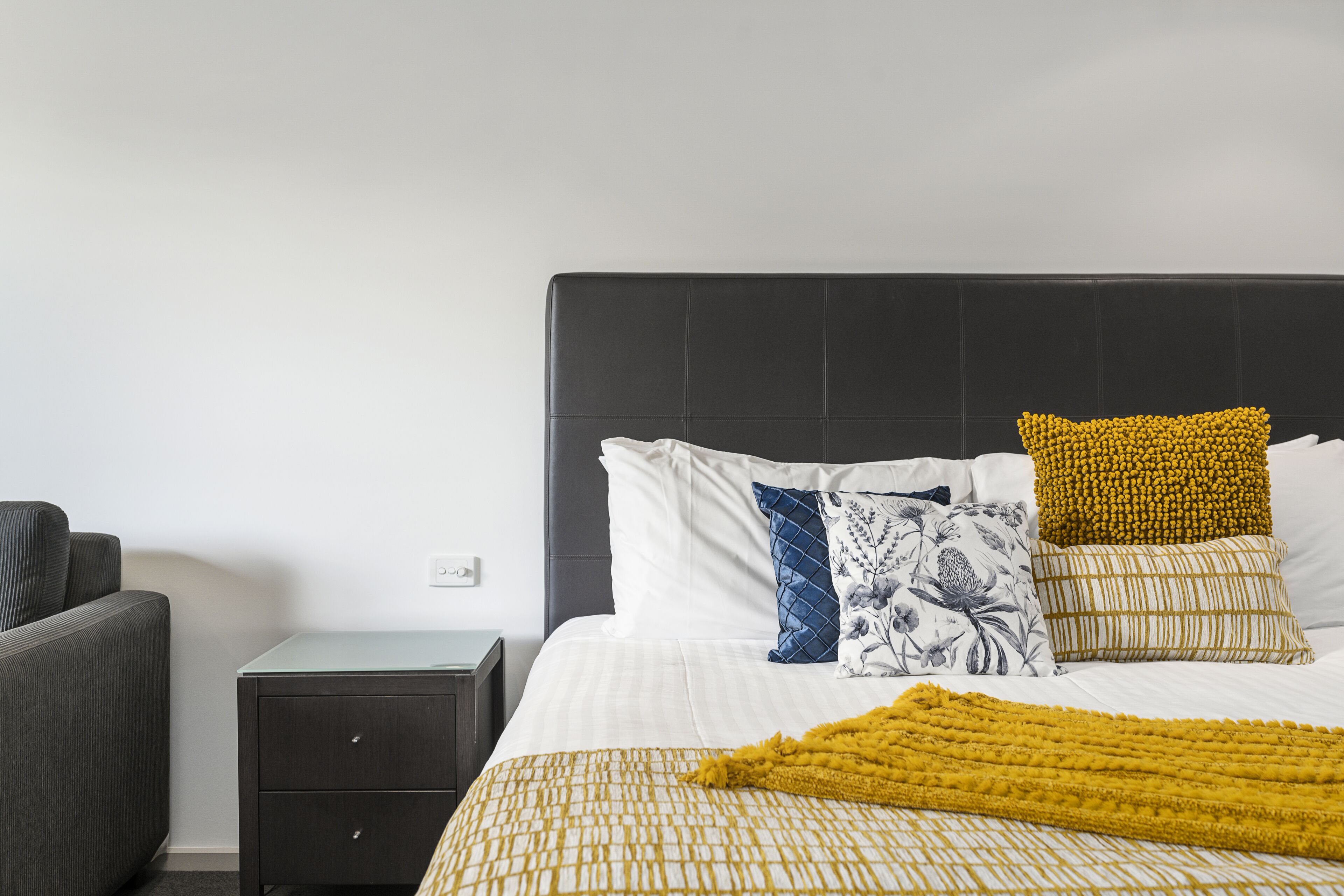 Een keurig ingerichte hotelkamer met een bed, een klein nachtkastje en een bank.