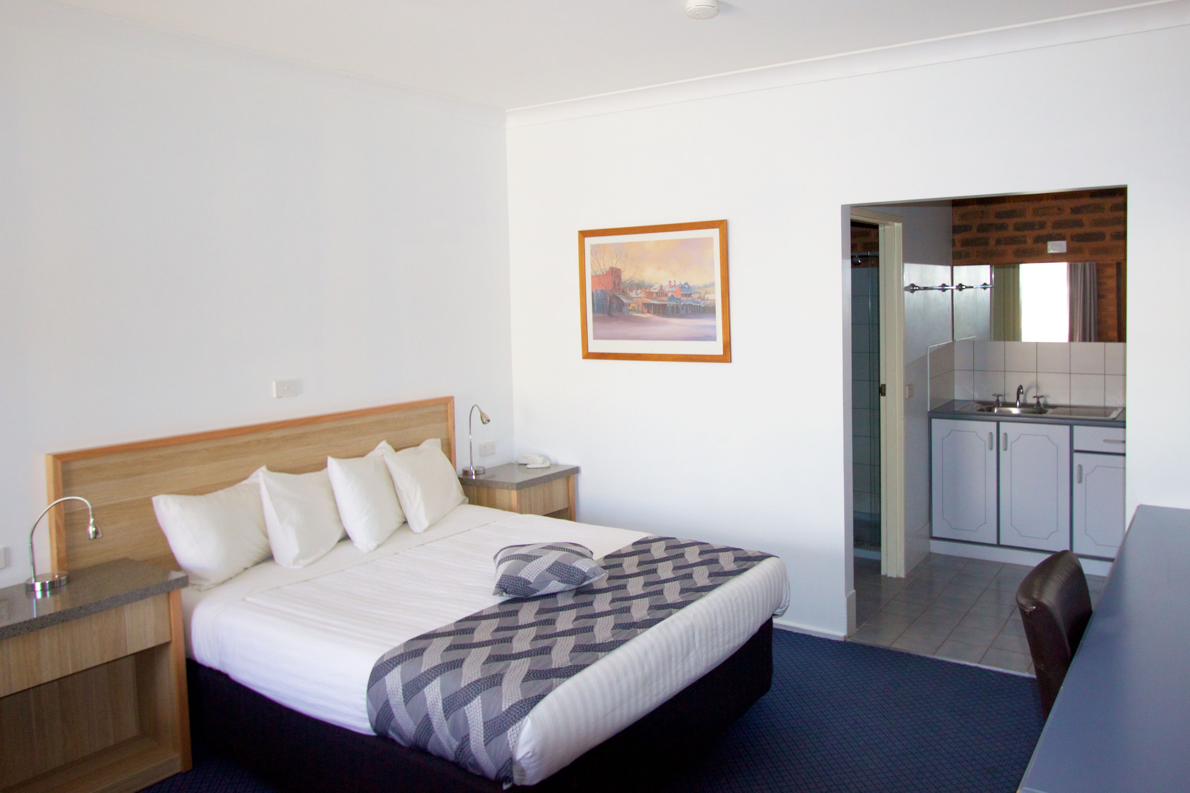 A hotel room with a bed, bedside table, lamp, and a painting on the wall.