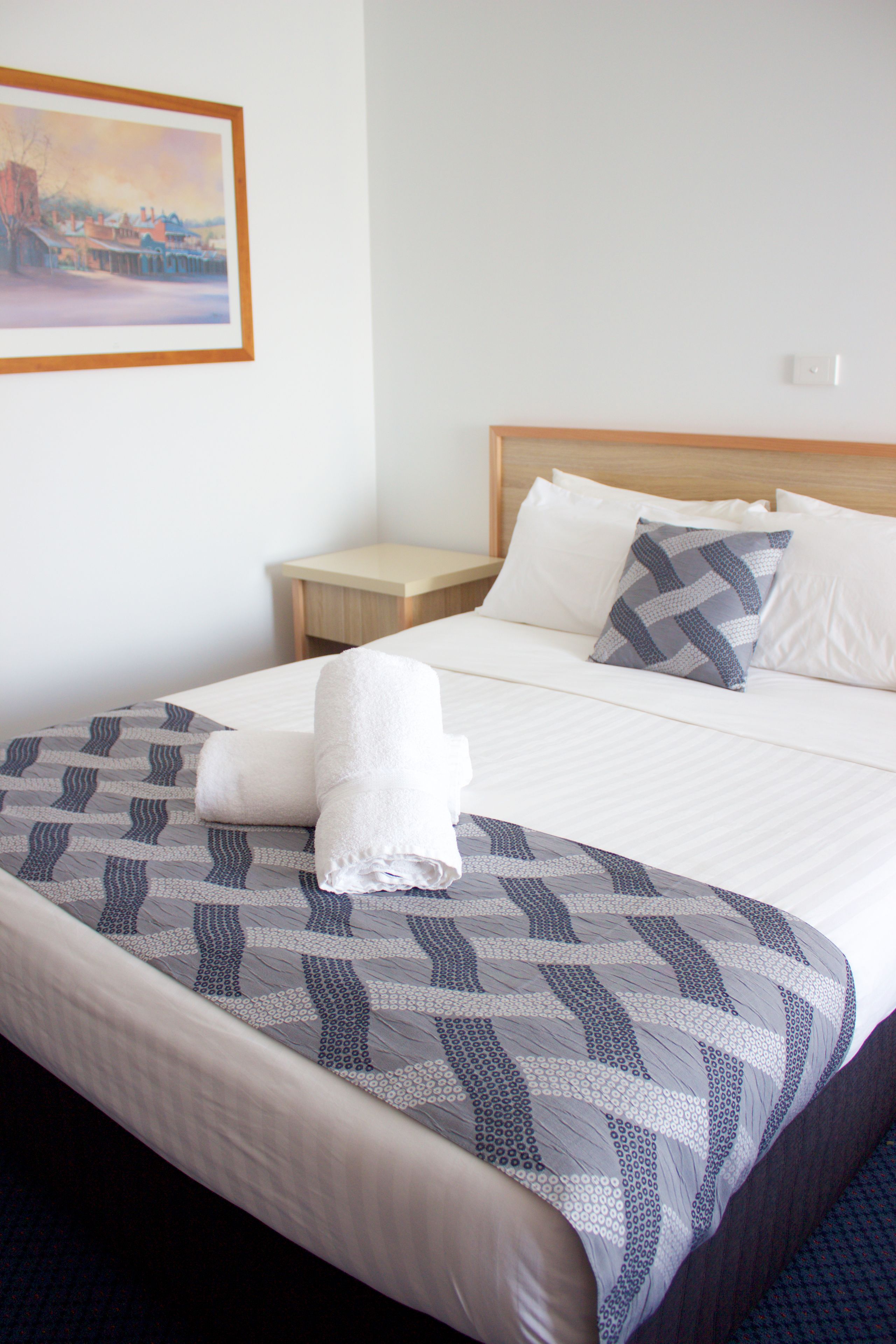 A neatly made bed with a patterned bedspread, two pillows, and a folded towel.