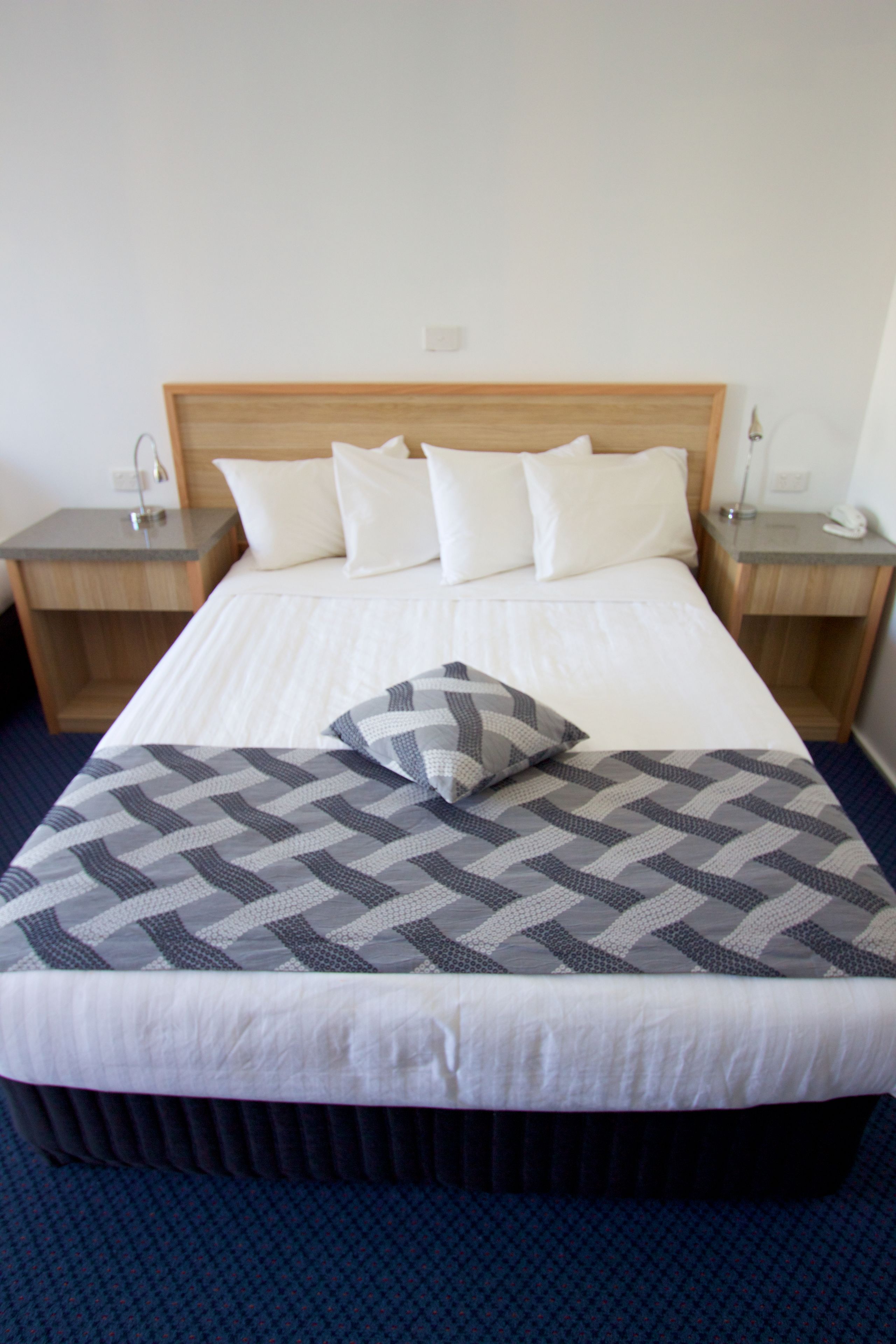 A neatly made bed with a checkered blanket and a pillow, flanked by two bedside tables with lamps, in a room with a simple, clean design.
