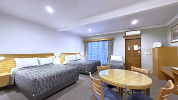 A hotel room with three beds, a dining table, and a wooden wardrobe.