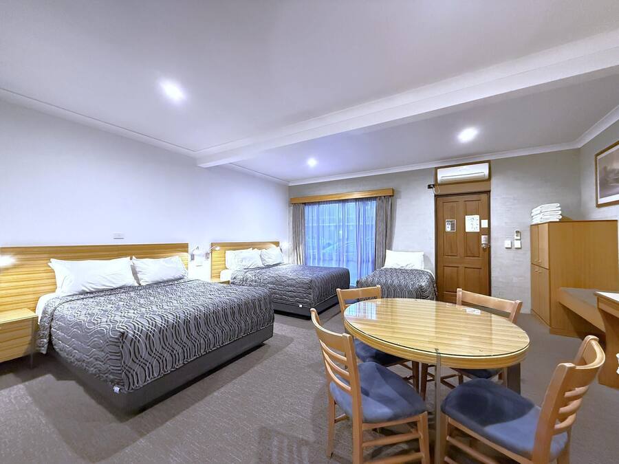 A hotel room with three beds, a dining table, and a wooden wardrobe.