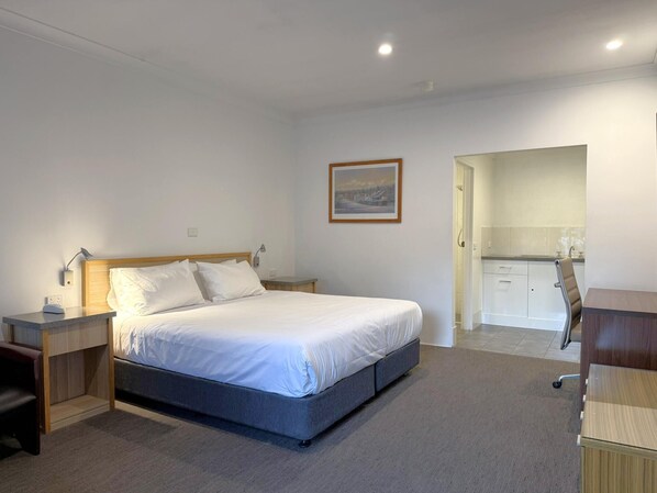 A bedroom with a bed, bedside tables, a desk, and a kitchenette.