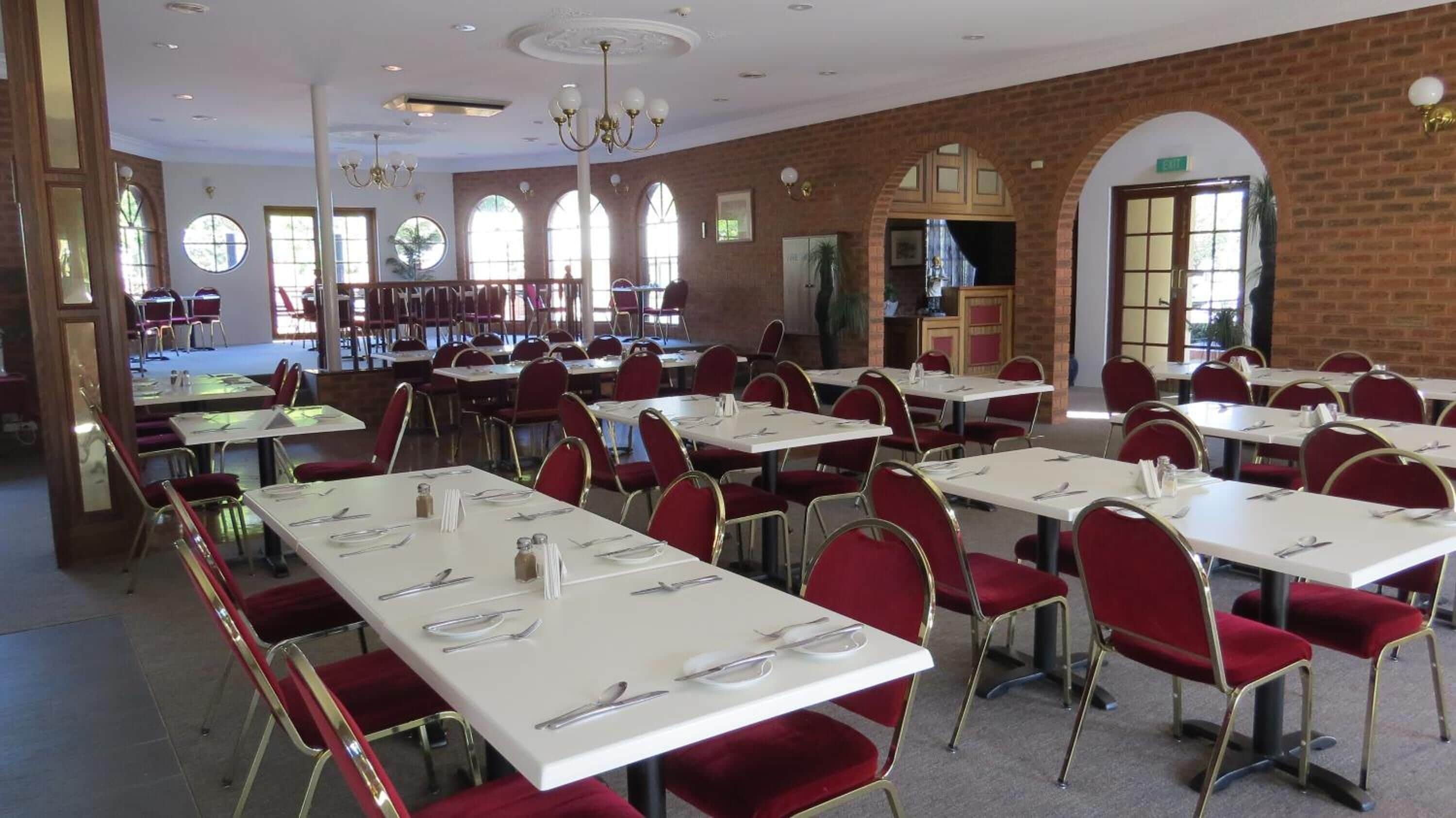 Un comedor amplio con varias mesas y sillas, ventanas grandes y una pared de ladrillo.