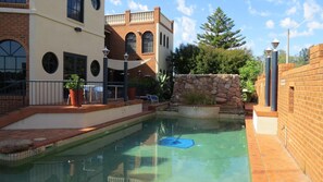 A swimming pool area with a stone wall, a lounge chair, and a building with arched windows. - Albury Paddlesteamer (South Albury)