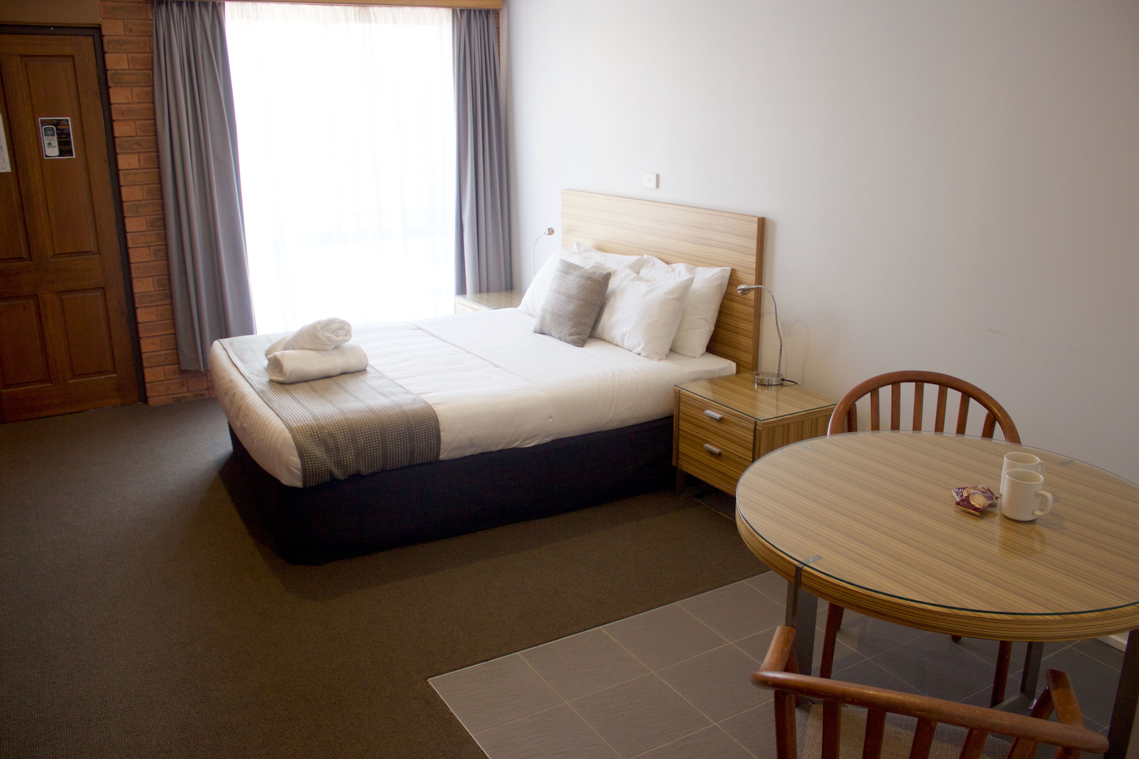 Habitación de hotel con cama, mesita de noche, una silla y una pequeña mesa con una taza.