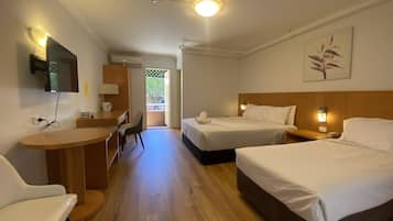 A hotel room with two beds, a desk, a chair, a TV mounted on the wall, and a door leading to an outdoor area.